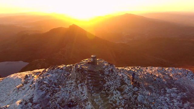 Tilting aerial shot of a climber eating on a mountain summit at sunrise.