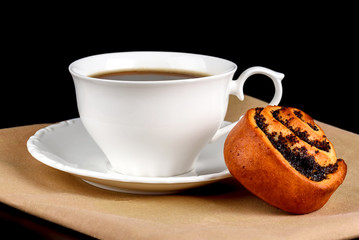A cup of coffee a bun with poppy seeds on a black background