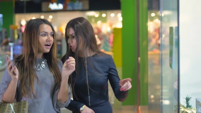 Ladies standing by the shopping window in the mall, emotionally discuss shopping. 4K.