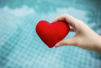 Fototapeta premium Valentine concept background, girl hand holding red heart over blue water background