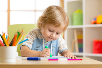 Kid little boy paints in his nursery at home