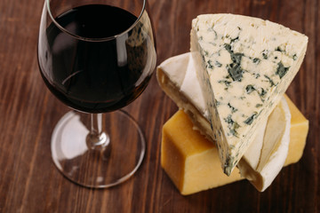 Delicious variety of cheese and a glass of red wine on old dark wooden table Top view 