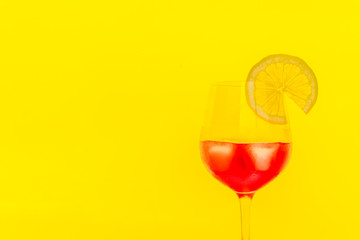 red cocktail with lemon slice and ice on yellow background