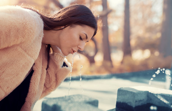 Thirsty woman drinking water from a fountain in the park
