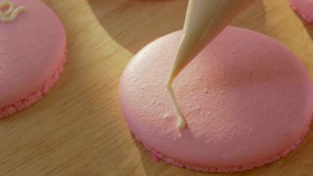Close-up on a pink macaroon biscuits or macaroon pastry does the inscription love , using a pastry bag. Decoration of confectionery products by 14 February. Romantic gift of love.