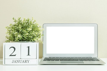 White wooden calendar with black 21 january word with white blank space at center of computer notebook on white wood desk and cream wallpaper textured background , selective focus at the calendar