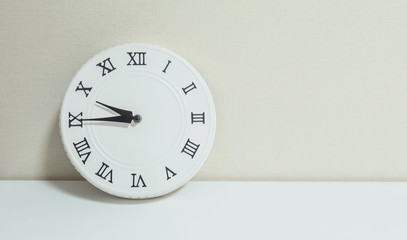 Closeup white clock for decorate show a quarter to ten or 9:45 a.m. on white wood desk and cream wallpaper textured background with copy space