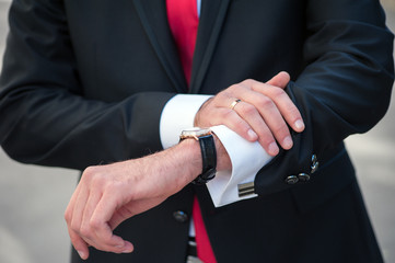 A man in a black suit straightens his cufflinks