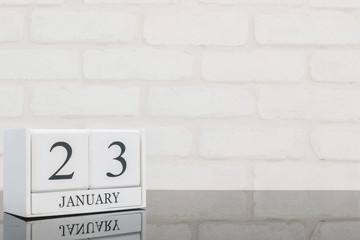 Closeup white wooden calendar with black 23 january word on black glass table and white brick wall textured background with copy space , selective focus at the calendar