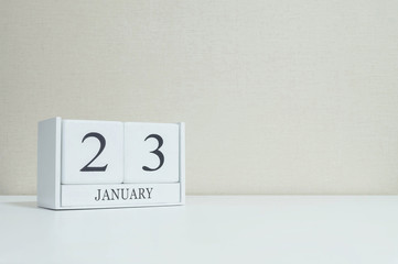 Closeup white wooden calendar with black 23 january word on blurred white wood desk and cream color wallpaper in room textured background with copy space , selective focus at the calendar