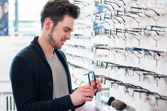 Mann als Kunde sucht Brille beim Optiker im Regal aus
