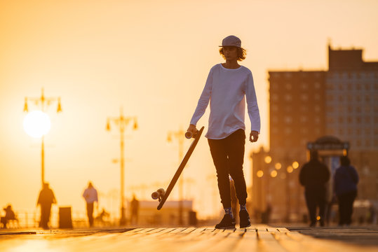 Young longboard rider silhouette walking on the boardwalk
