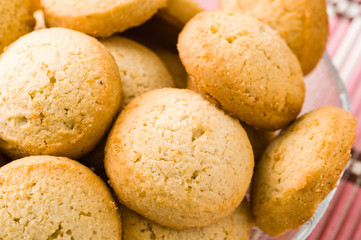Tasty golden brown cardamom biscuits in small glass bowl on pink tablecloth.