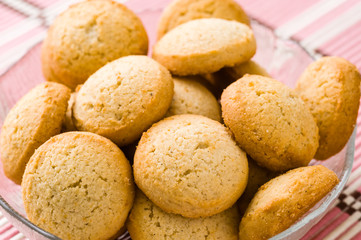 Tasty golden brown cardamom biscuits in small glass bowl on pink tablecloth.
