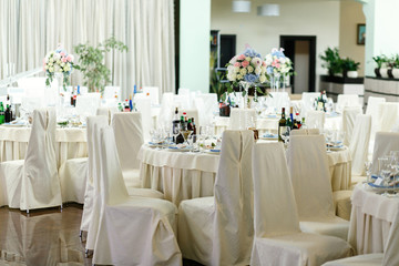 Chairs covered with white cloth stand at little round dinner tab