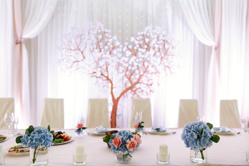 Blue hydrangeas in glasses stand on long white dinner table