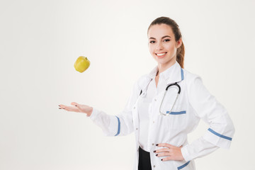 Happy woman doctor standing and throwing apple in the air