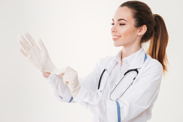 Cheerful attractive young woman doctor puttin on rubber gloves