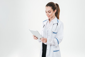 Smiling attractive young woman doctor standing and using tablet
