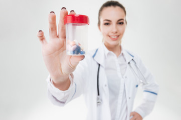 Cheerful pretty young woman doctor showing bottle of pills