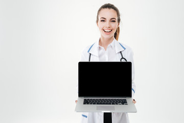 Cheerful pretty young woman doctor holding blank screen laptop