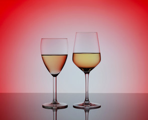 Two wineglasses with white wine on blurred red background