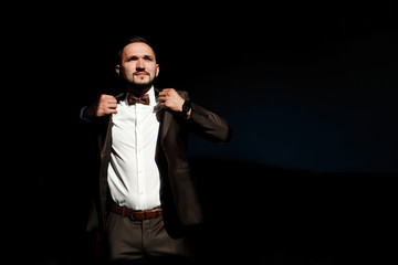 Handsome man puts on his jacket standing in the ray of light amo