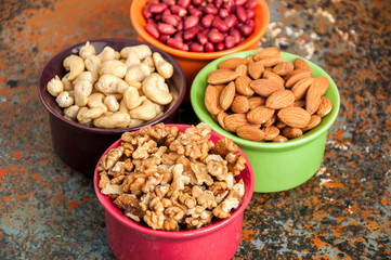 Set of variety of nuts. Almond, peanuts, walnuts and cashew in color ceramic bowls on a rusty background