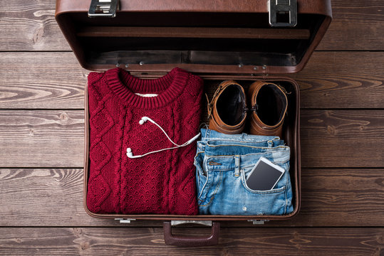 Open suitcase with casual female winter clothes on wooden table. Top view