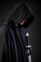 Portrait of a courageous warrior wanderer in a black cloak and sword in hand. - obrazy, fototapety, plakaty