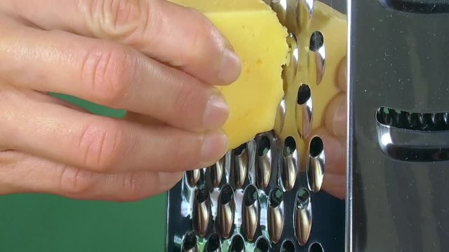 Closeup of a woman grating holand cheese on green background