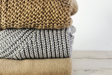 three warm sweaters in a stack on a white wooden shelf on a ligh