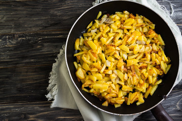 Fried potatoes in a frying pan on a wooden background in rustic style