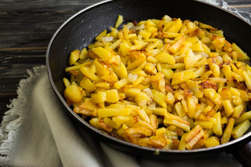 Fried potatoes in a frying pan on a wooden background in rustic style