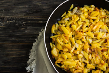 Fried potatoes in a frying pan on a wooden background in rustic style