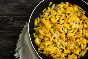 Fried potatoes in a frying pan on a wooden background in rustic style