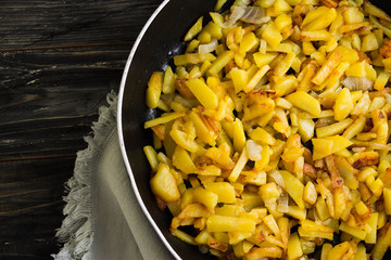 Fried potatoes in a frying pan on a wooden background in rustic style