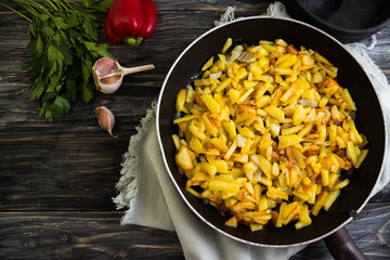 Fried potatoes in a frying pan on a wooden background in rustic style