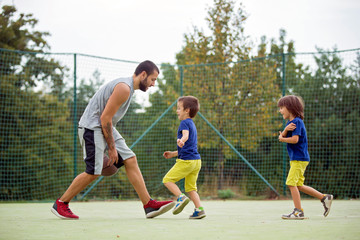 Fototapeta premium Young children, brothers and their father, playing basketball