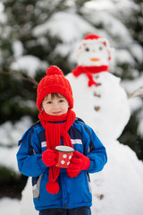 Happy beautiful child building snowman in garden