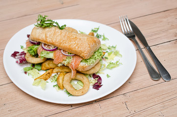 Salmon sandwich with salad, fries and onion rings