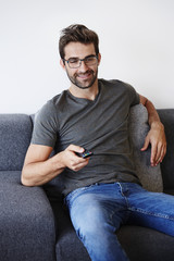 Guy with emote control on sofa, smiling