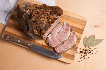 Sliced baked pork with herbs and spice on wooden board.