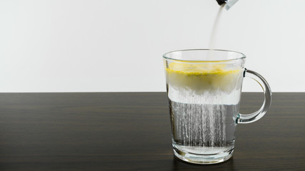 Ein Glas mit Wasser auf einem dunklen Holztisch mit weißem Hintergrund und Textfreiraum, in das Wasser wird aus einem Tütchen Pulver geschüttet
