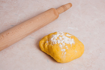 Rolling pin and yellow dough with white flour on light marble ba