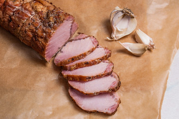 Close up view of sliced smoked meat or ham and garlic on brown p