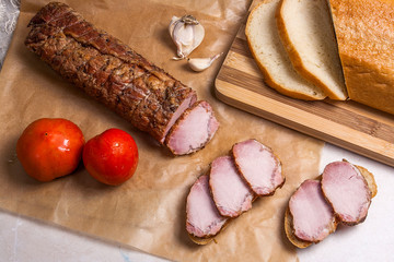 Slices smoked meat or ham on brown packing paper. Tomatoes, garl