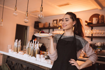 Cheerful young woman confectioner holding cake in hands.
