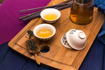 Green herbal tea in glass teapot on the blue wood background with aroma sticks and tea cup