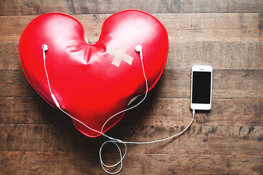 red broken heart with bandage listening music on mobile phone, Broken heart concept on wood floor